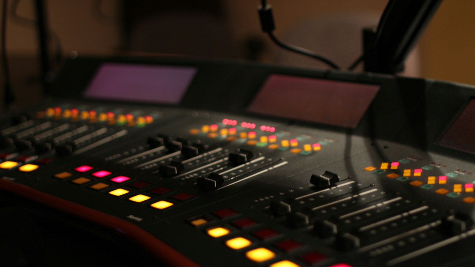 A lit broadcast on air console in a radio studio with the mic boom overhead, the kind of room a radio station consultant assesses in the first week