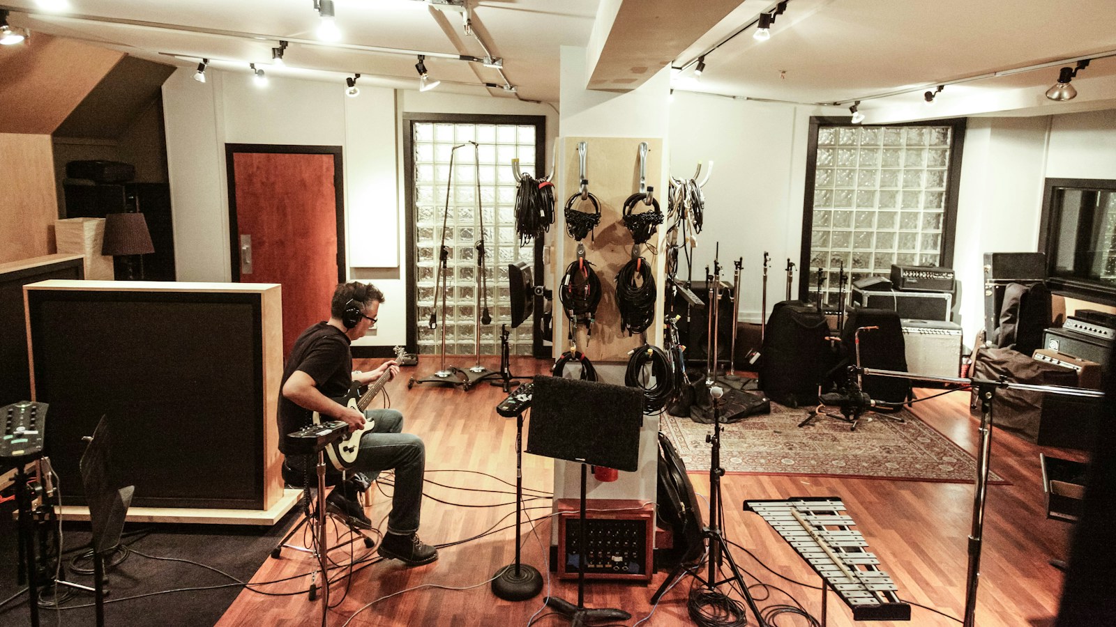 A musician tracking in a recording studio live room with microphone stands, headphone cables and amplifiers staged, the kind of session where a radio jingle package gets re-sung