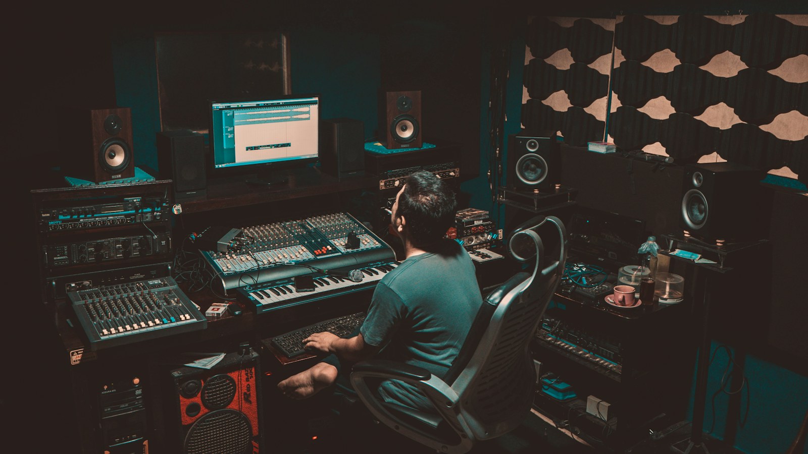 A producer at a studio console mixing a session on screen with studio monitors and acoustic treatment, the room where a radio commercial actually gets built