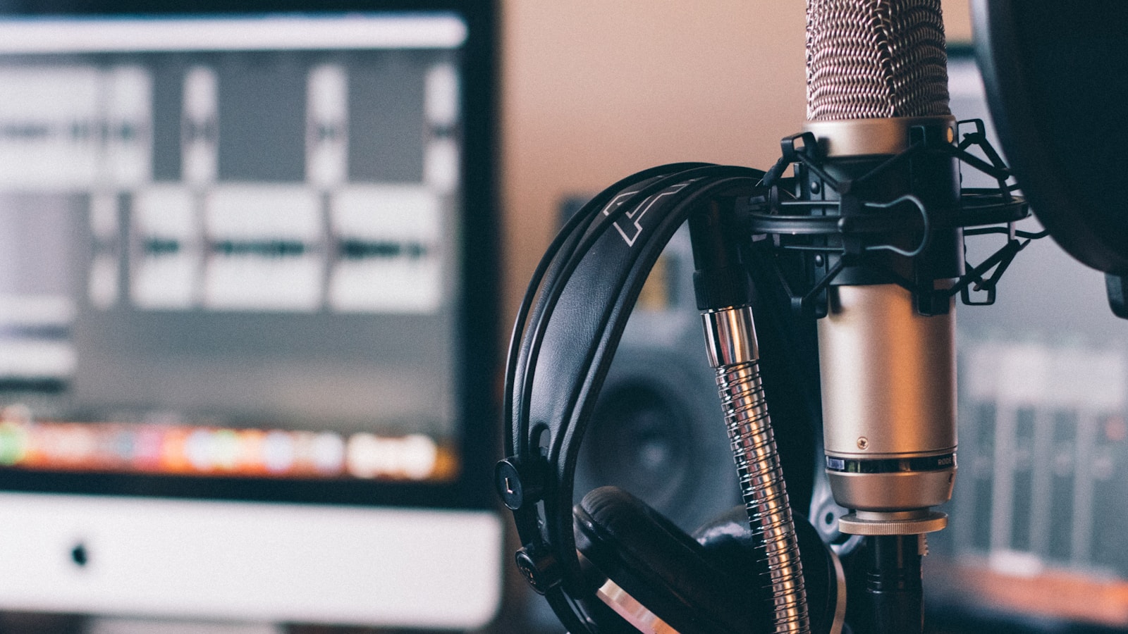 Studio condenser microphone and headphones in front of a screen of recorded audio tracks, a working setup for voice tracking a radio shift