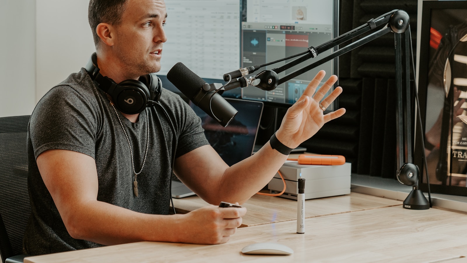 Radio talent mid-break at a broadcast microphone with a music log and audio session open on the screens behind him, the daily execution a radio consultant reviews first